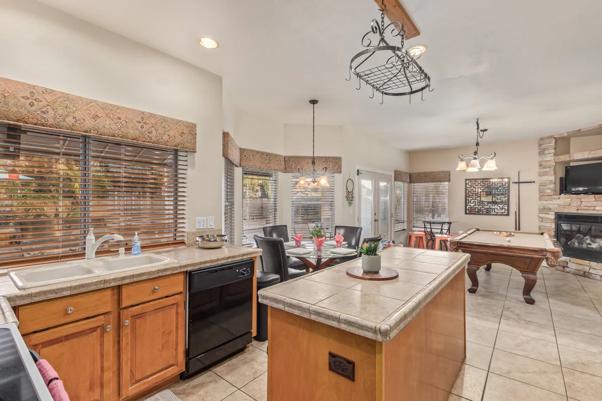A vibrant and welcoming interior showcases a large kitchen island, a connected dining area, a pool table, and a fireplace. The design flows seamlessly from one activity space to another, highlighting both culinary and recreational features in an inviting, resort-style setting.