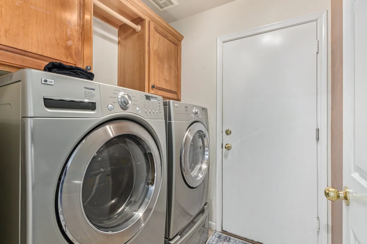 This image showcases a dedicated laundry room featuring a washing machine, drying machine, ample wooden cabinetry for storage, and a clean white door. The space is organized and well-lit, conveying efficiency and convenience for handling laundry tasks during extended stays.
