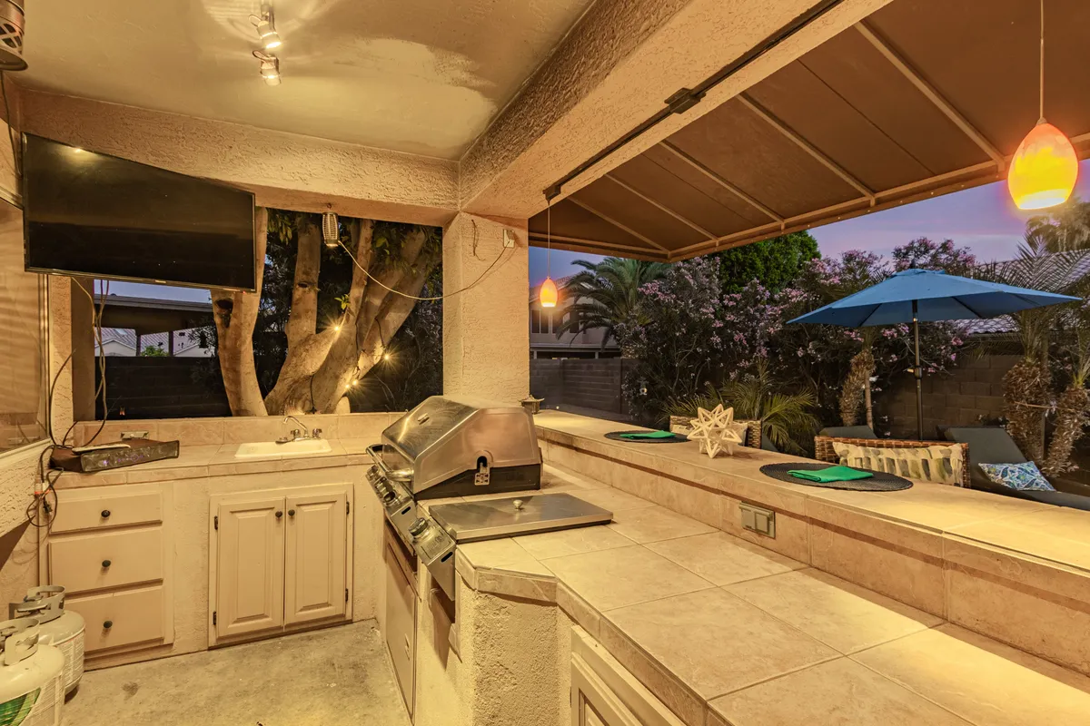 The outdoor kitchen area, complete with a large grill, bar seating, decorative elements, and a sun umbrella, encourages al fresco dining and entertaining. The setting is ideal for post-golf gatherings, barbecues, and enjoying meals while taking in the surrounding outdoors.