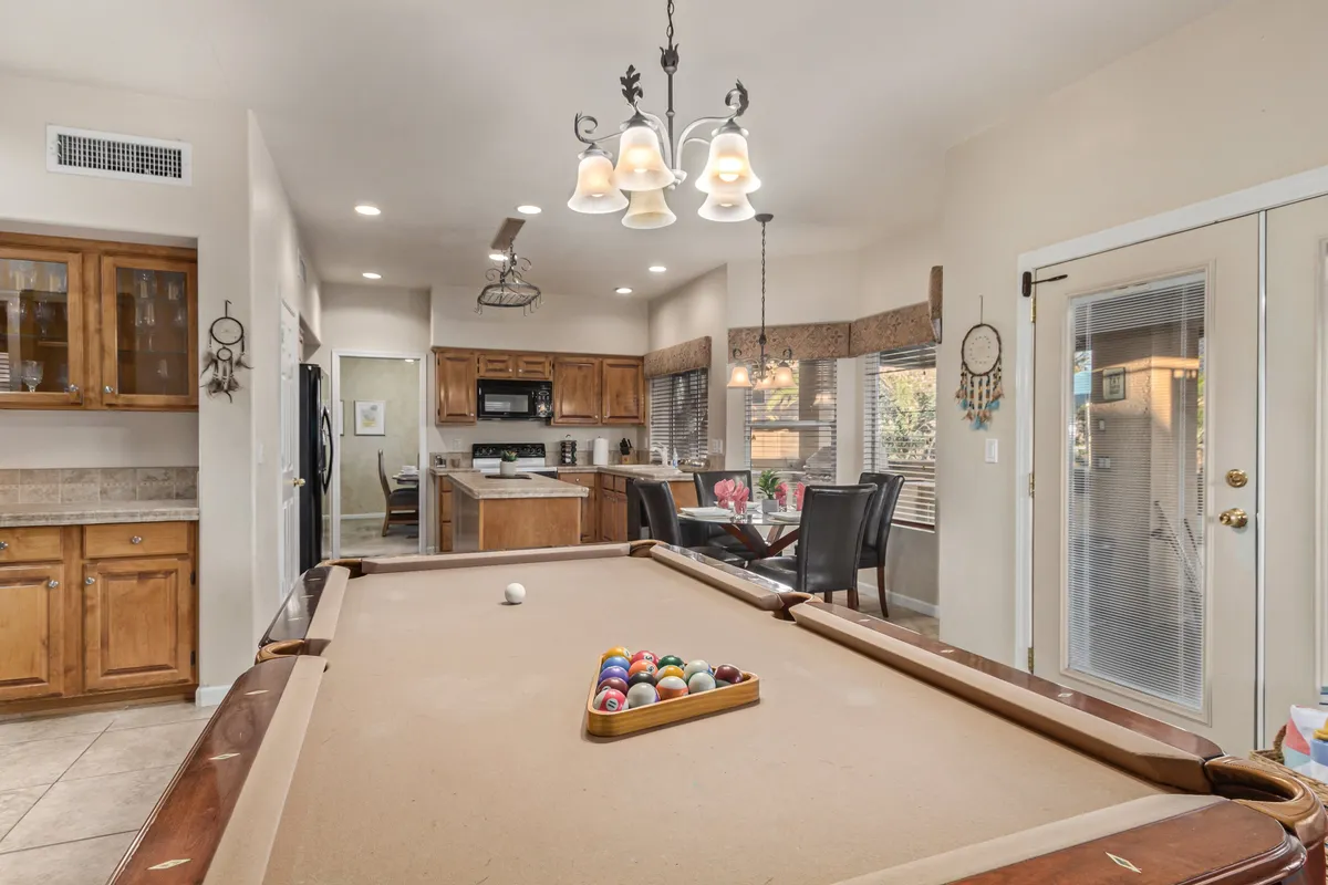 This image displays a spacious open-plan area that prominently features a pool table, a dining area, and an adjacent kitchen area. Natural light floods the space, while the arrangement encourages socializing and group activities. The kitchen and dining spaces are seamlessly connected to the game area, creating an ideal environment for various entertaining scenarios.