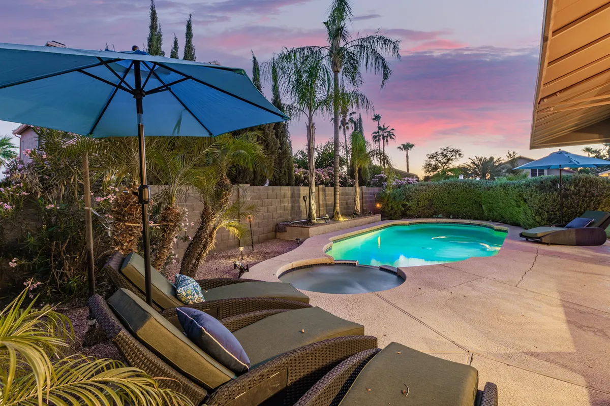 A serene pool area with luxury loungers shaded by an umbrella, palm trees swaying gently nearby, and the warm glow of sunset reflecting off the water. The setting invites guests to relax, sunbathe, or enjoy the tranquil atmosphere at any time of day.