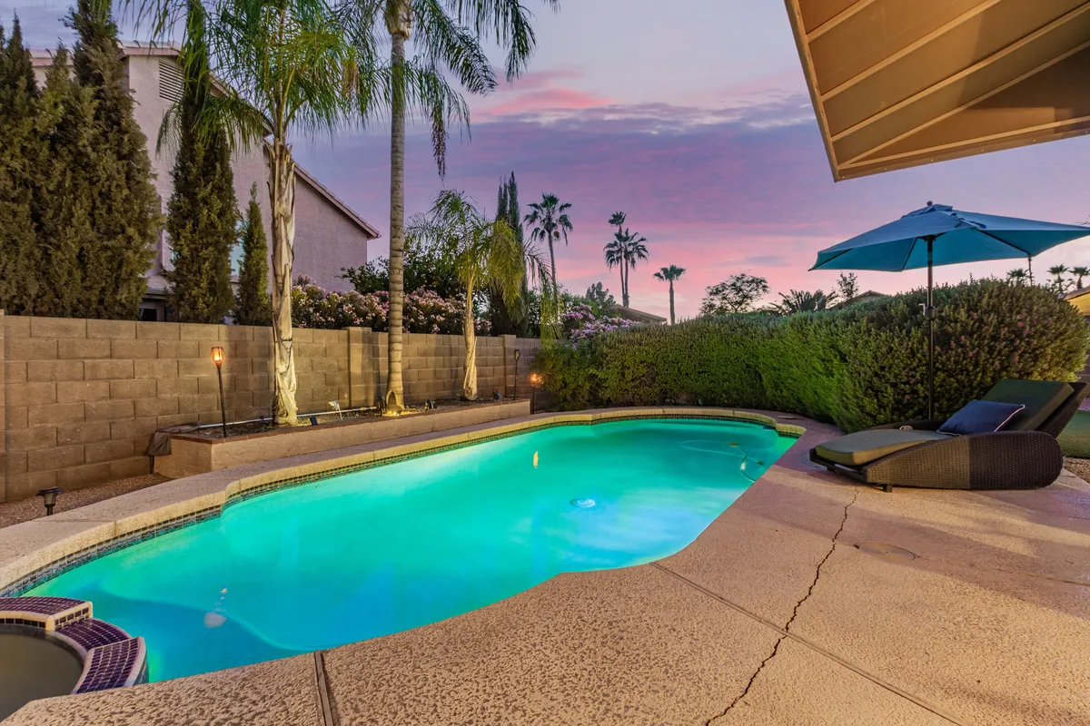 A striking exterior view of the swimming pool, lounge chair, palm trees, and a colorful sunset sky. The mood is peaceful and rejuvenating, inviting guests to unwind in style after a productive day.