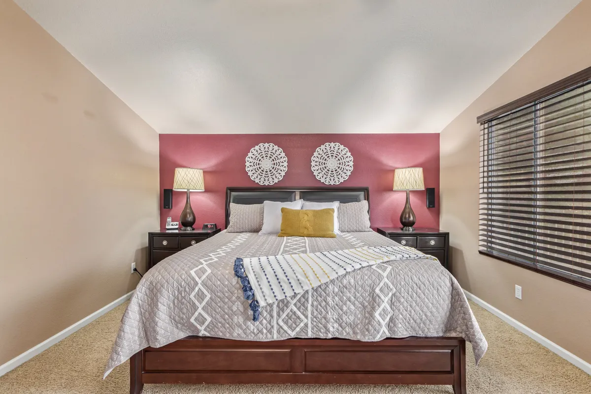 A serene bedroom with a bed adorned with decorative pillows, soft lighting from bedside lamps, and tasteful wall art. The tranquil mood is accentuated by the gentle natural light streaming in, creating an atmosphere of restful privacy and style.