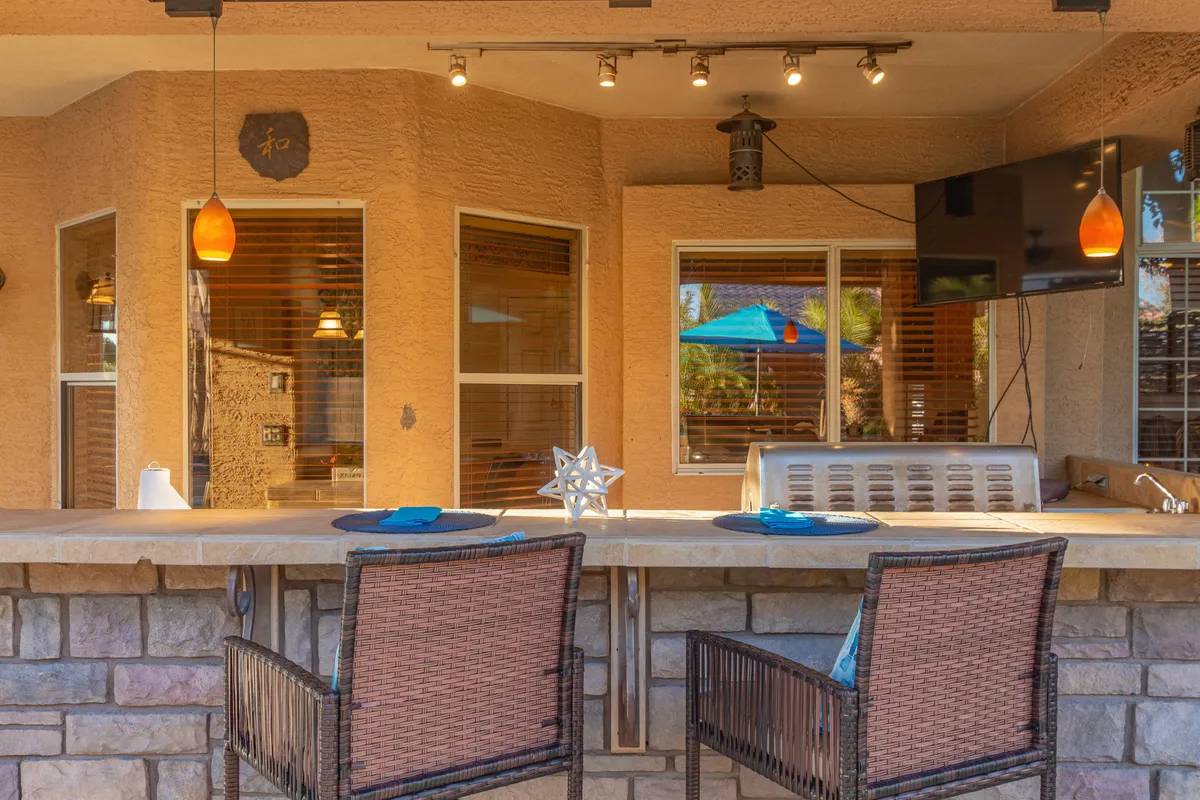 A stylish bar counter with hanging light fixtures, a television, and blue decorative accents set the scene for casual entertainment and sports viewing. The inviting setup is ideal for serving drinks, watching the game, or enjoying relaxed social interactions.