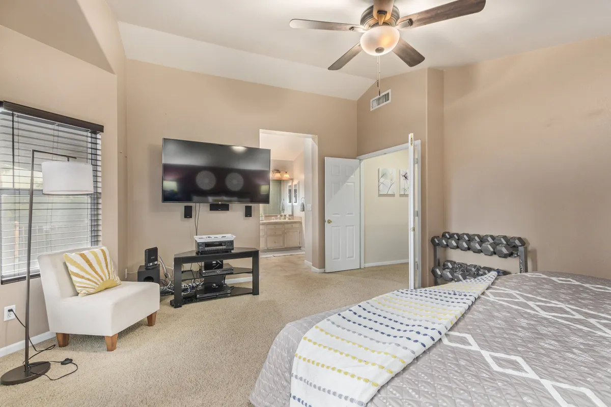 A spacious bedroom with a large bed and decorative pillows, a cozy seating area, and a television. There is a visible doorway leading to an ensuite bathroom, making the space ideal for comfort and convenience. The mood is comfortable and homely, perfect for recharging.