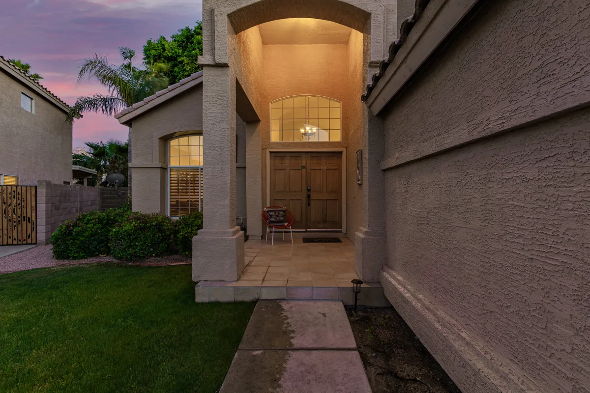 The entrance porch of the home features comfortable seating, a welcoming door, and a chandelier, all bathed in warm light. The scene evokes feelings of hospitality and sets the tone for a relaxing stay.