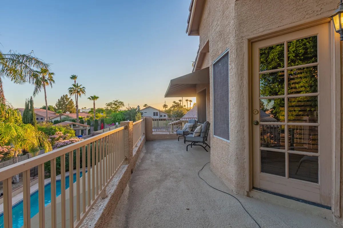 A serene balcony with a railing overlooks a sparkling pool, comfortable seating, and lush greenery, all set against a stunning sunset sky. The tranquil mood invites relaxation after a day of golf, with panoramic sunset views and a peaceful, resort-like vibe.