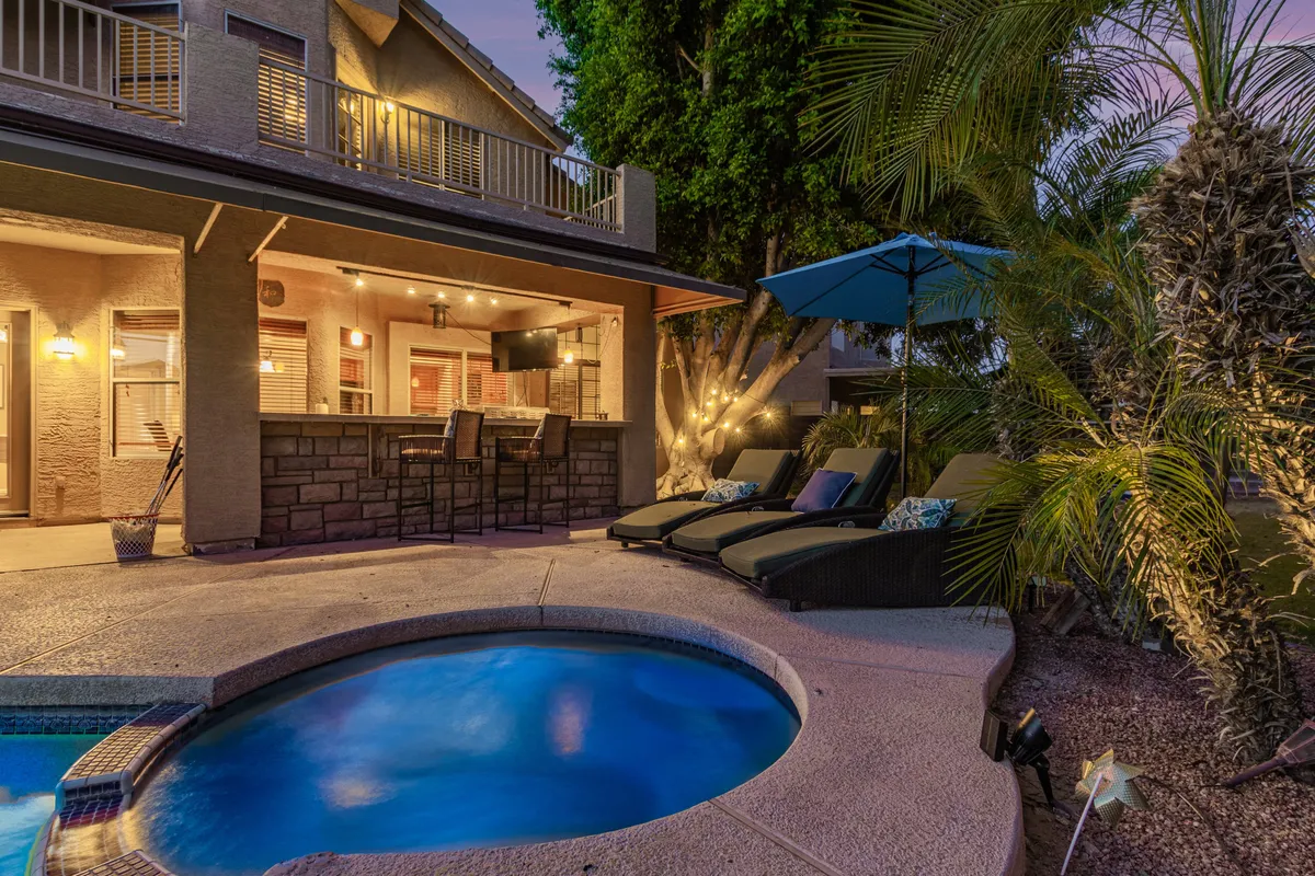 The image showcases a sparkling swimming pool surrounded by comfortable outdoor seating and a barbecue station, all accented by soft, inviting outdoor lighting. The setting is ideal for poolside gatherings, relaxed evenings, and entertaining friends, with ample space for both activity and relaxation. The sunset glow over the pool creates a tranquil and festive mood.