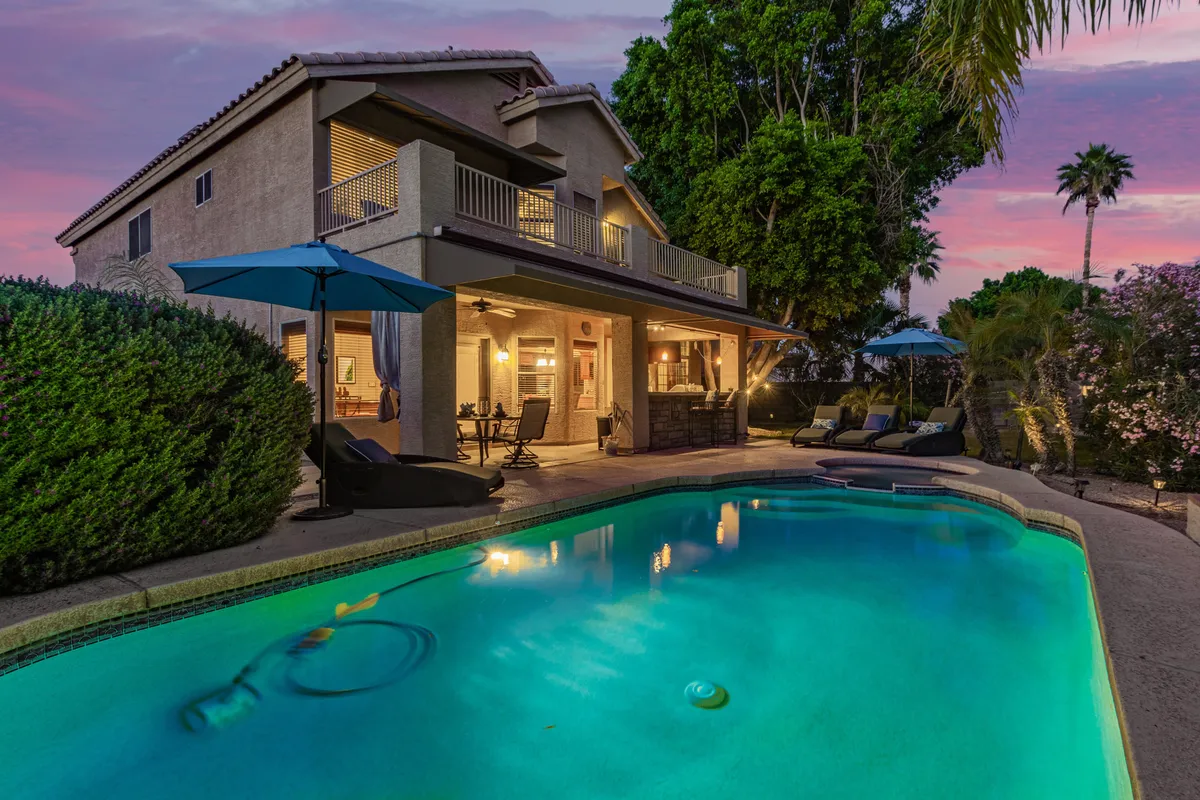 This image features a spacious backyard with a sparkling swimming pool, comfortable outdoor seating, a balcony, and lush greenery surrounding the area. The setup suggests opportunities for swimming, socializing, and relaxing in a serene, sunlit environment ideal for all ages.